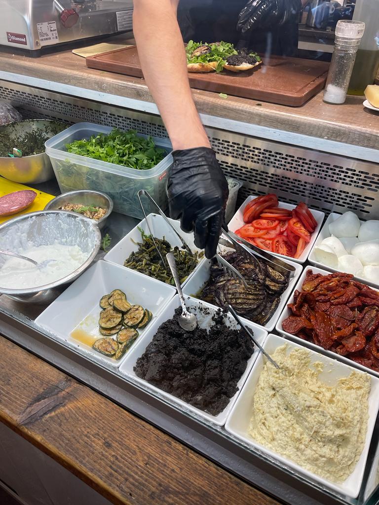 A person preparing a Italian sandwich